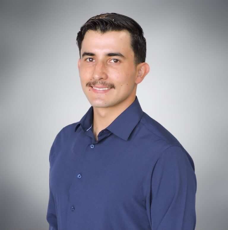 Professional profile photo of the family real estate partner wearing a blue collared shirt against a grey gradient background, representing traditional home sale services