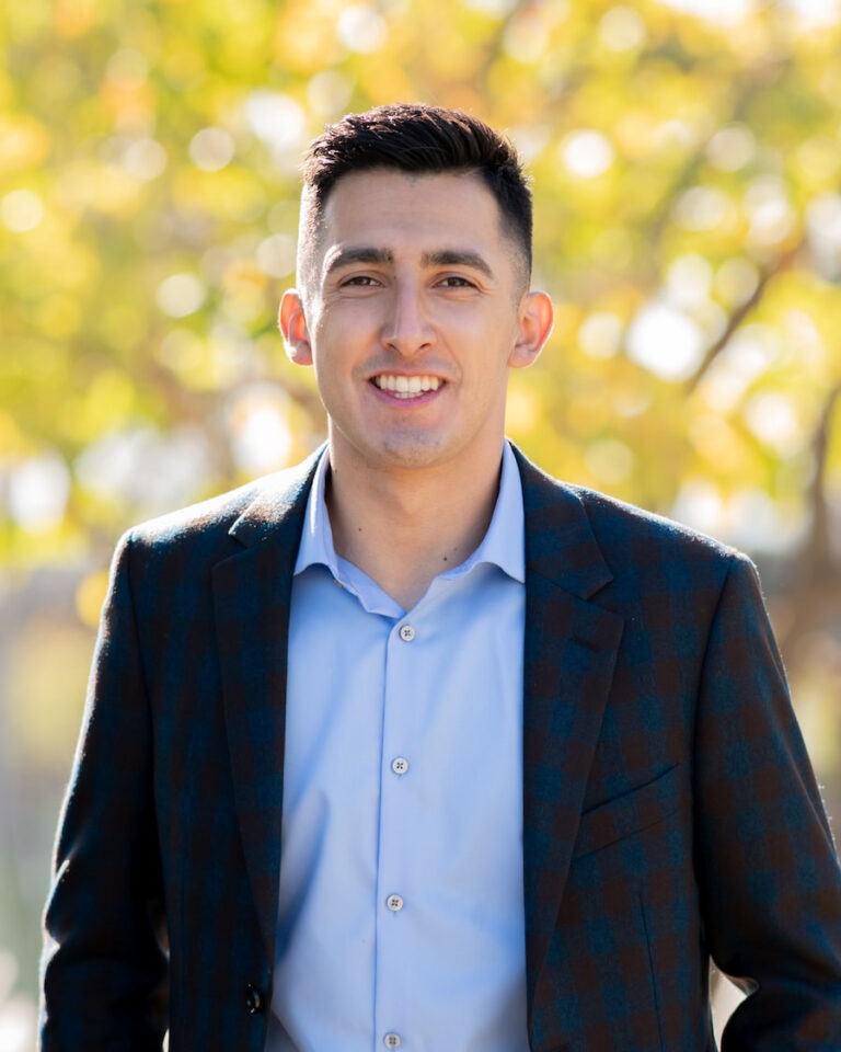 Professional profile photo of the owner of Exclusive SoCal Home Buyers, who loves to serve SoCal homeowners, smiling in business attire with a blurred outdoor background