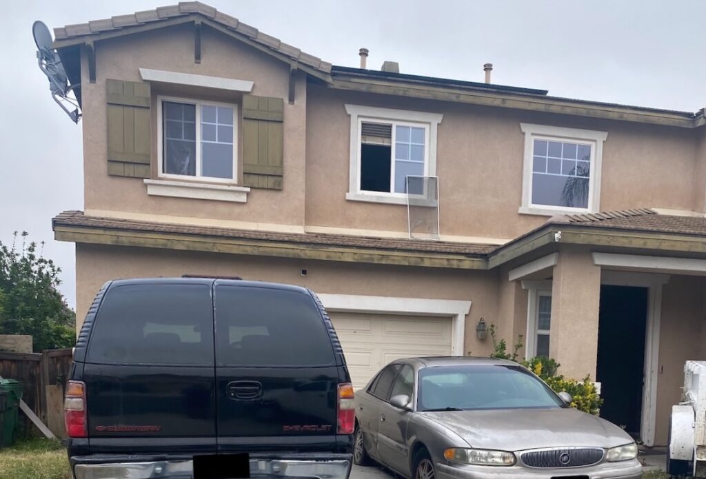 Two-story stucco house on Peacock Mountain Drive in Menifee with vehicles in the driveway and a worn exterior before the as-is sale